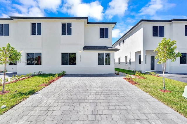 view of front of home with stucco siding, decorative driveway, and a front lawn