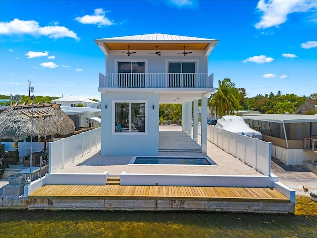 back of house featuring a ceiling fan, a balcony, stucco siding, fence private yard, and metal roof
