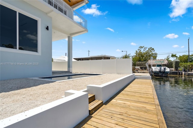 dock area with fence, a water view, and a balcony