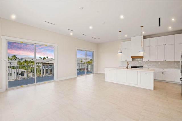 kitchen featuring tasteful backsplash, a sink, a center island with sink, light countertops, and white cabinets