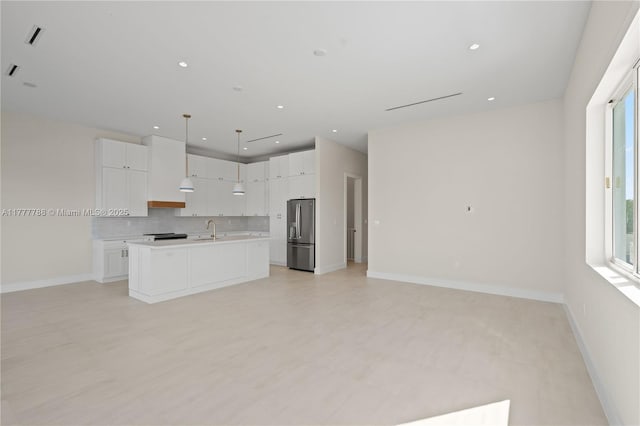 kitchen with backsplash, light countertops, a sink, stainless steel fridge, and open floor plan