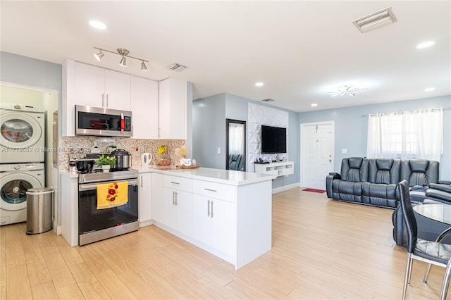 kitchen with visible vents, open floor plan, a peninsula, stacked washer and dryer, and stainless steel appliances