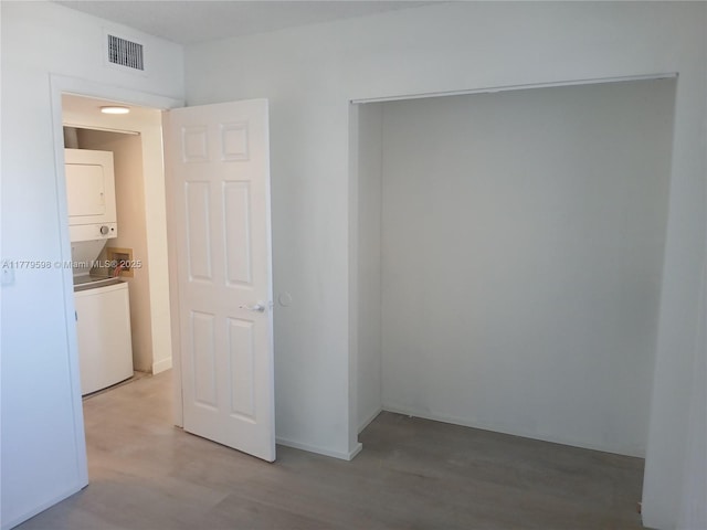 interior space featuring stacked washer / drying machine, visible vents, and light wood-style flooring