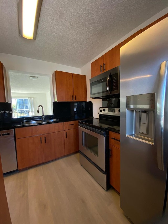 kitchen with dark countertops, light wood-style floors, stainless steel appliances, and a sink