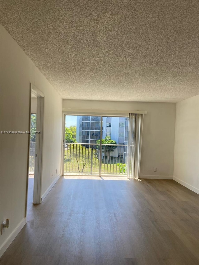 unfurnished room with wood finished floors, a textured ceiling, and baseboards