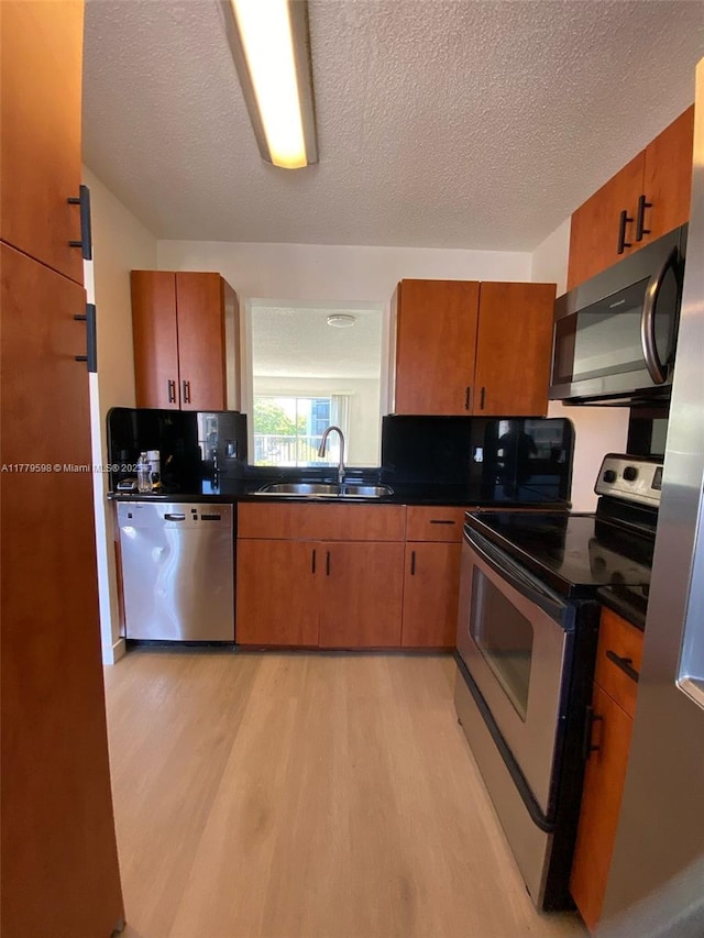 kitchen with stainless steel appliances, a textured ceiling, a sink, dark countertops, and light wood-style floors