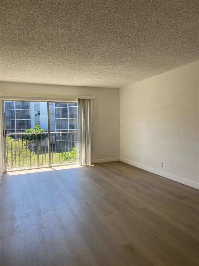 unfurnished room with baseboards, wood finished floors, and a textured ceiling