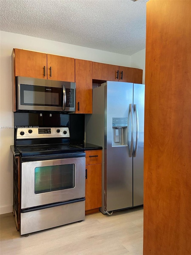 kitchen with brown cabinets, stainless steel appliances, a textured ceiling, and light wood-style floors