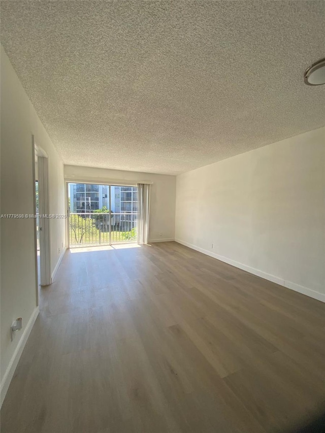 empty room featuring dark wood-type flooring, a textured ceiling, and baseboards