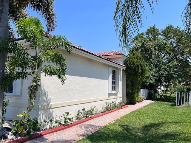 view of side of home featuring a tiled roof, stucco siding, and a lawn