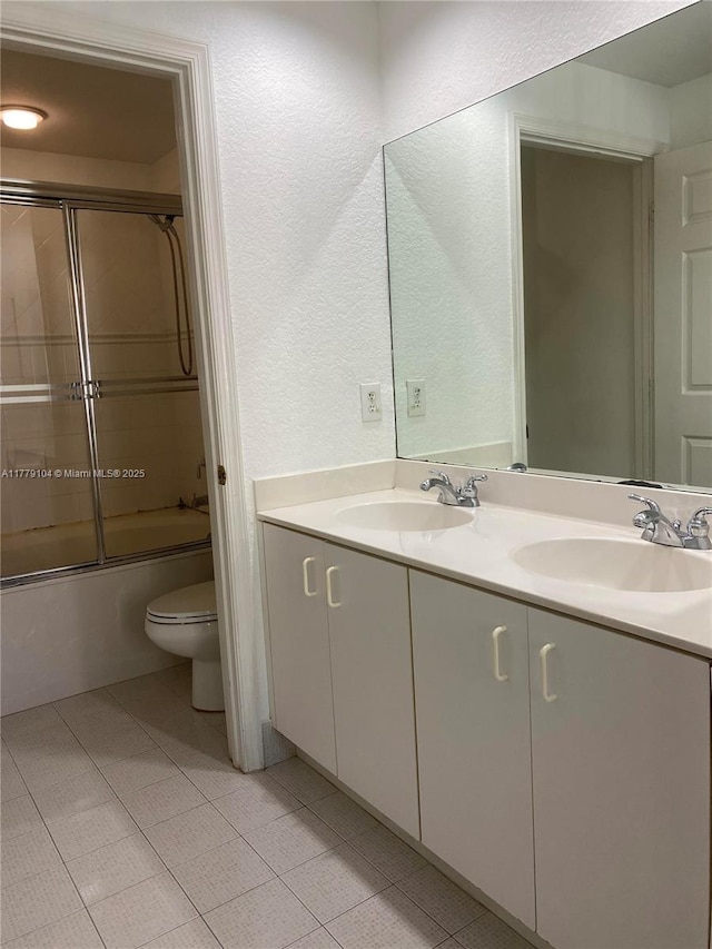 bathroom with toilet, double vanity, a textured wall, and a sink