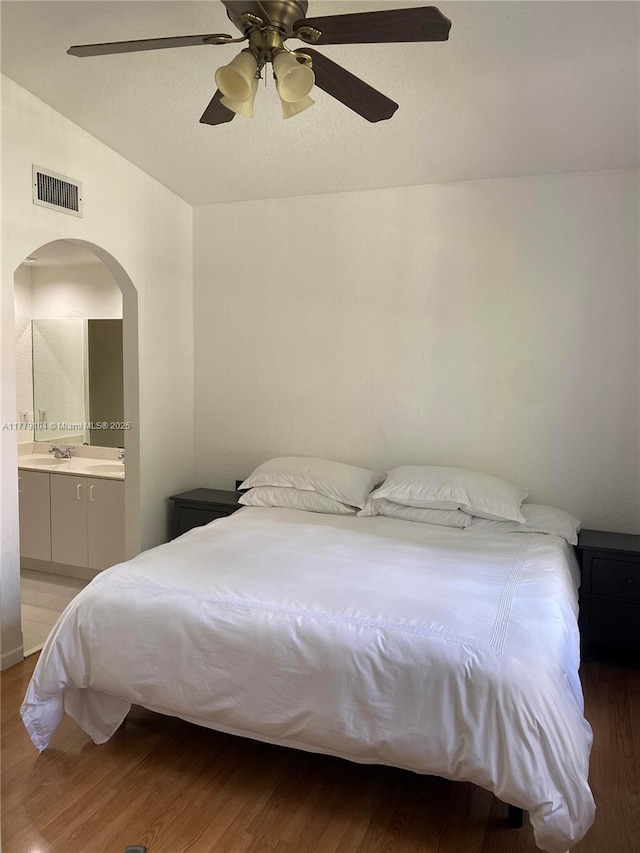 bedroom with vaulted ceiling, ensuite bathroom, light wood-style flooring, visible vents, and arched walkways