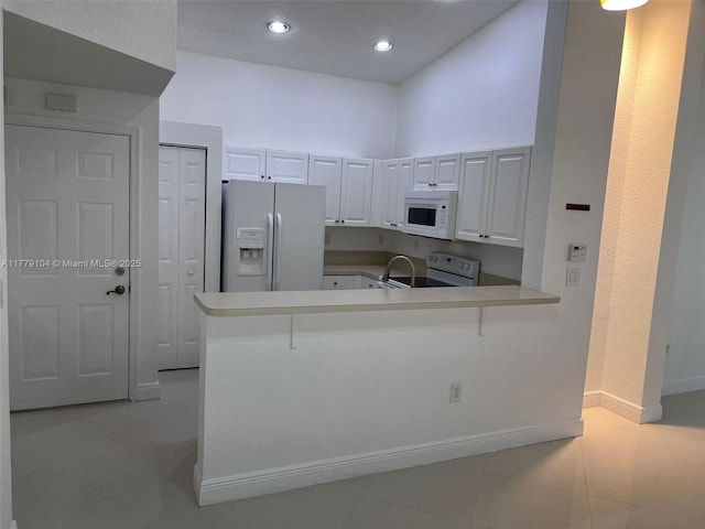 18769 SW 28th St, Miramar, FL 33029 - kitchen with white appliances, a peninsula, light tile patterned floors, baseboards, and white cabinets