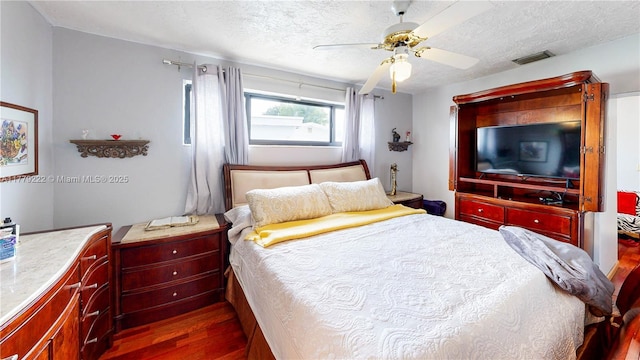 bedroom featuring dark wood-style floors, a textured ceiling, visible vents, and ceiling fan