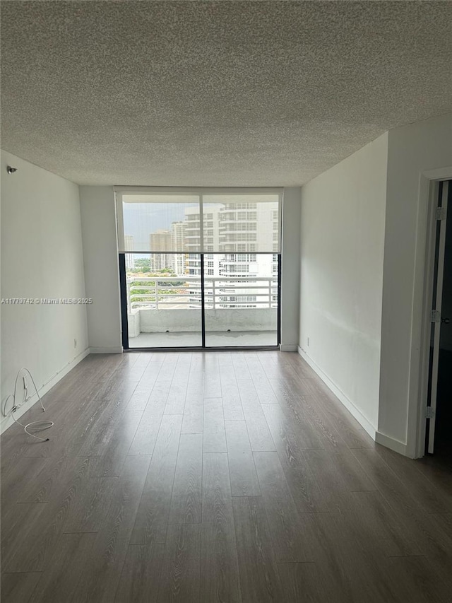 empty room featuring a textured ceiling, a healthy amount of sunlight, wood finished floors, and a wall of windows