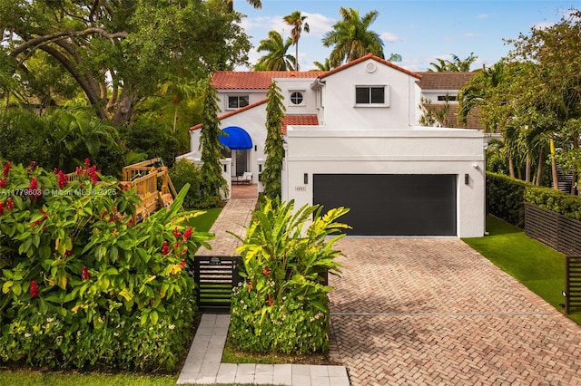 mediterranean / spanish-style house featuring a garage, stucco siding, a tile roof, and decorative driveway