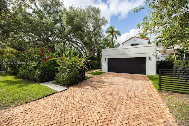 exterior space with a front yard, an attached garage, fence, stucco siding, and decorative driveway