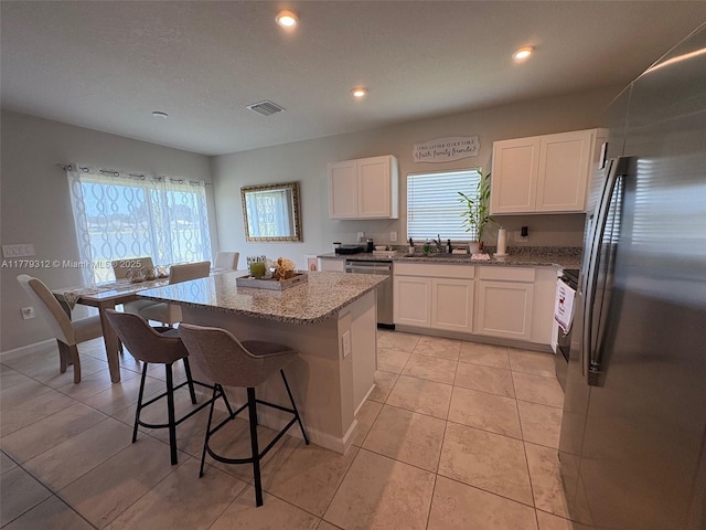 kitchen featuring a sink, visible vents, appliances with stainless steel finishes, a kitchen island, and light stone counters