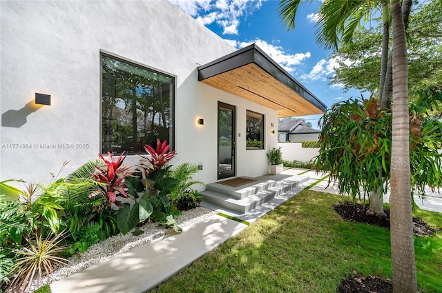 rear view of house featuring a yard, fence, and stucco siding