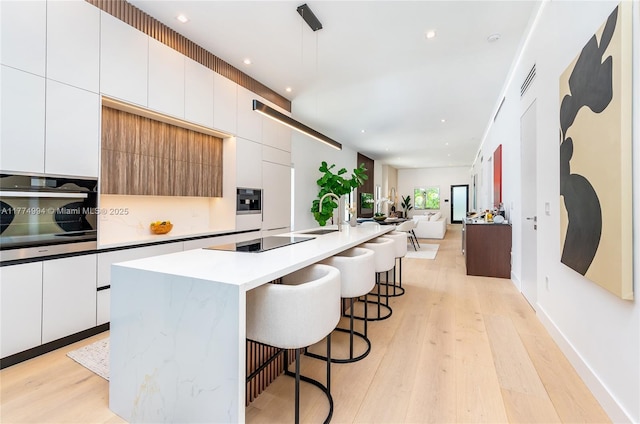 kitchen with stainless steel oven, light wood finished floors, black electric stovetop, and modern cabinets