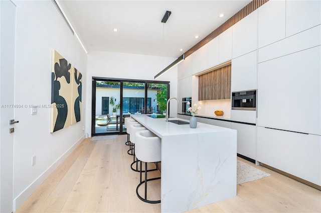 kitchen with light wood-type flooring, a breakfast bar, modern cabinets, and a center island with sink