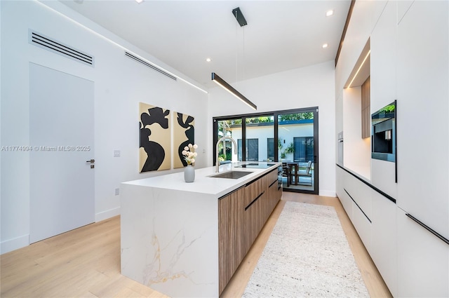 kitchen featuring modern cabinets, a sink, a kitchen island with sink, light wood finished floors, and white cabinetry