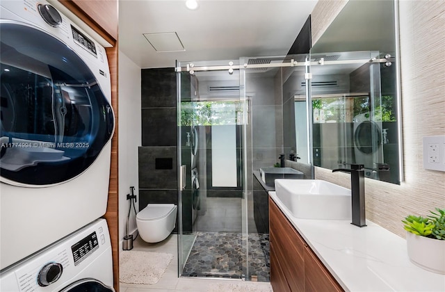 bathroom featuring toilet, stacked washing maching and dryer, a shower stall, vanity, and tile patterned floors