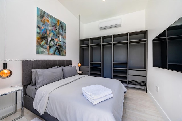 bedroom with an AC wall unit, baseboards, and wood finished floors
