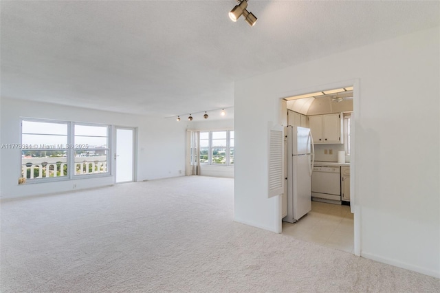 unfurnished living room with track lighting, baseboards, and light colored carpet