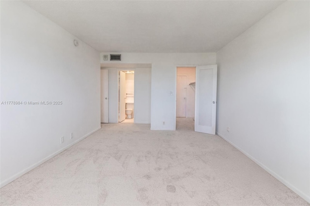unfurnished bedroom with a walk in closet, baseboards, carpet, and visible vents