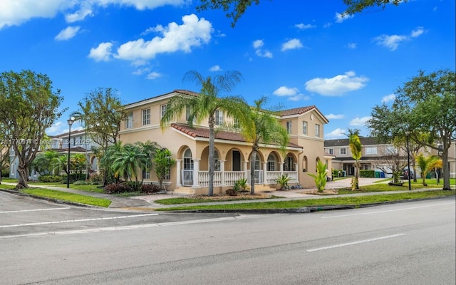 mediterranean / spanish house with a tiled roof, covered porch, and stucco siding
