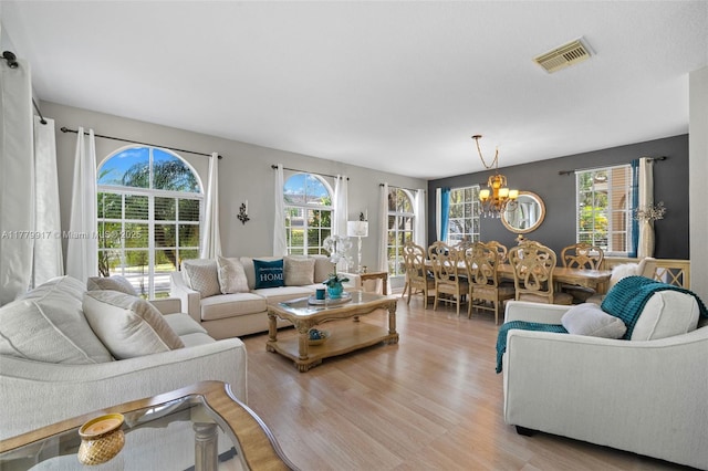 living area featuring visible vents, light wood-style flooring, and a notable chandelier