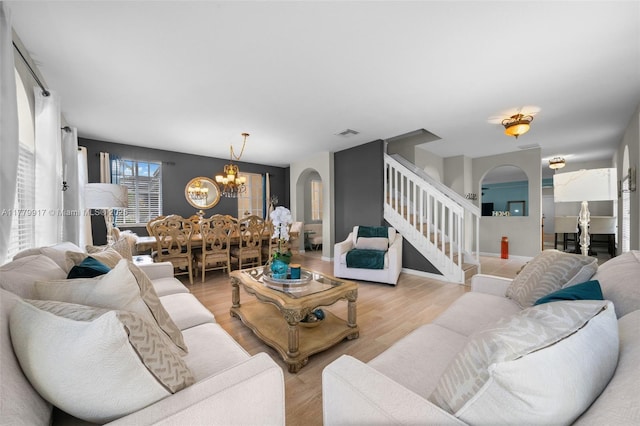 living room featuring a chandelier, stairway, visible vents, arched walkways, and light wood finished floors