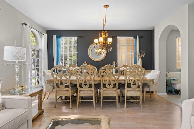 dining space featuring arched walkways, a notable chandelier, and wood finished floors