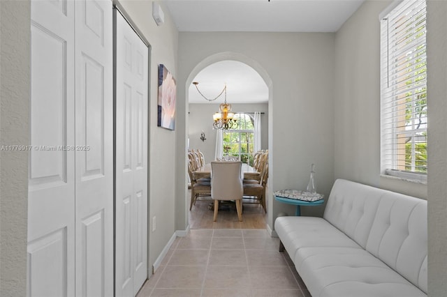 interior space featuring arched walkways, light tile patterned floors, baseboards, and an inviting chandelier