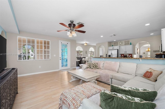 living room featuring visible vents, baseboards, arched walkways, ceiling fan, and light wood finished floors