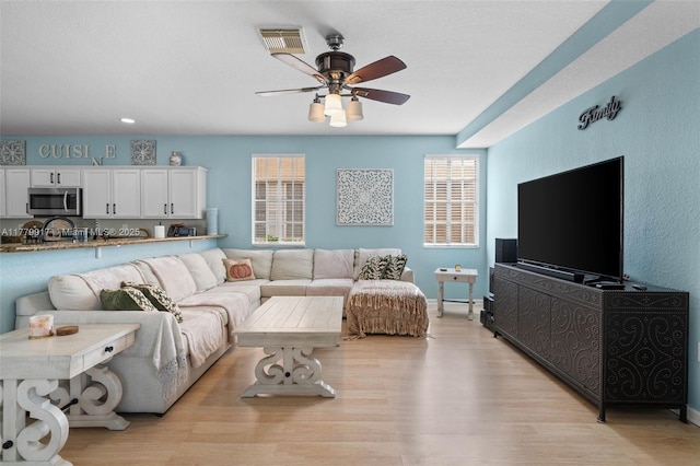 living area with visible vents, ceiling fan, a wealth of natural light, and light wood-style floors
