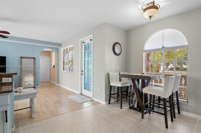dining space featuring arched walkways, ceiling fan, baseboards, and plenty of natural light