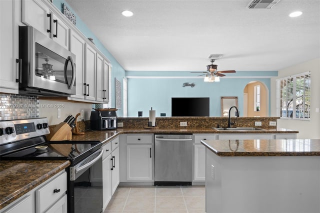 kitchen with a peninsula, light tile patterned floors, ceiling fan, stainless steel appliances, and a sink
