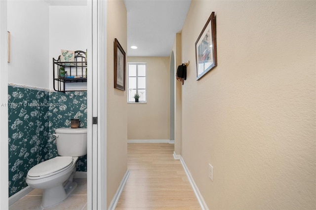bathroom with toilet, wood finished floors, baseboards, and wallpapered walls