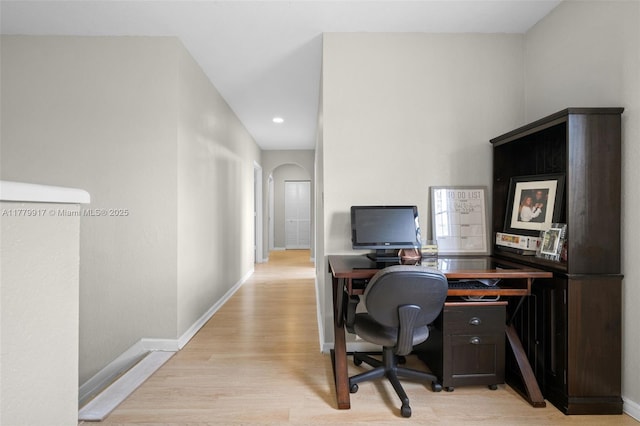 office area with baseboards, light wood finished floors, and arched walkways