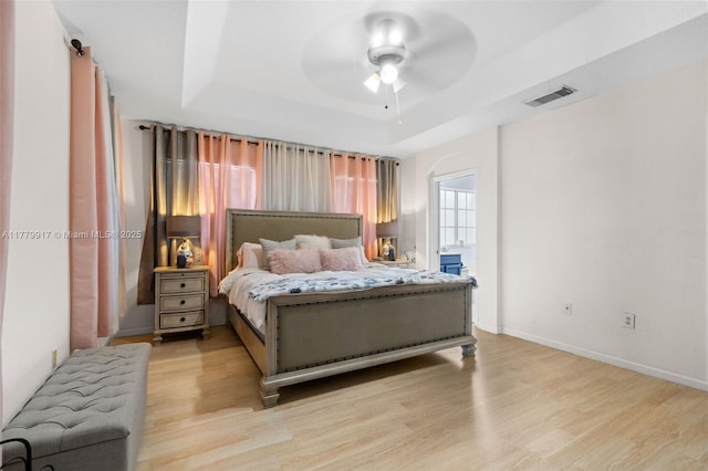 bedroom featuring visible vents, baseboards, a ceiling fan, a tray ceiling, and light wood-style flooring
