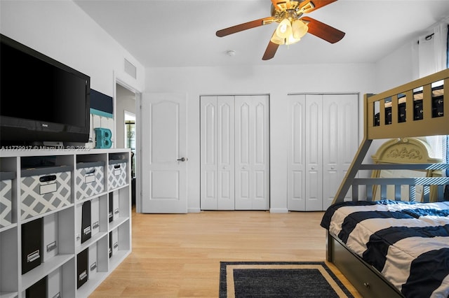 bedroom featuring light wood-style flooring, visible vents, multiple closets, and a ceiling fan