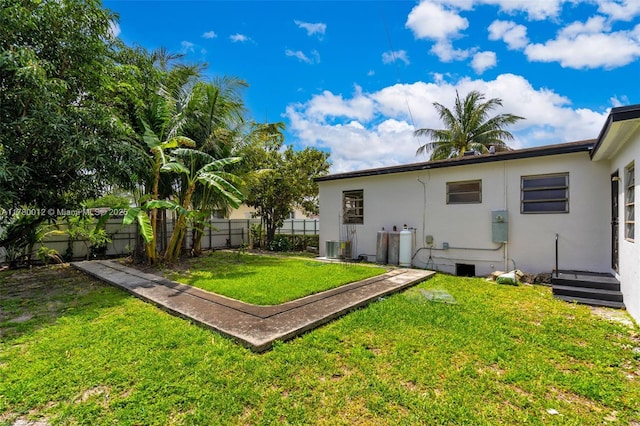 rear view of property featuring stucco siding, fence, and a lawn