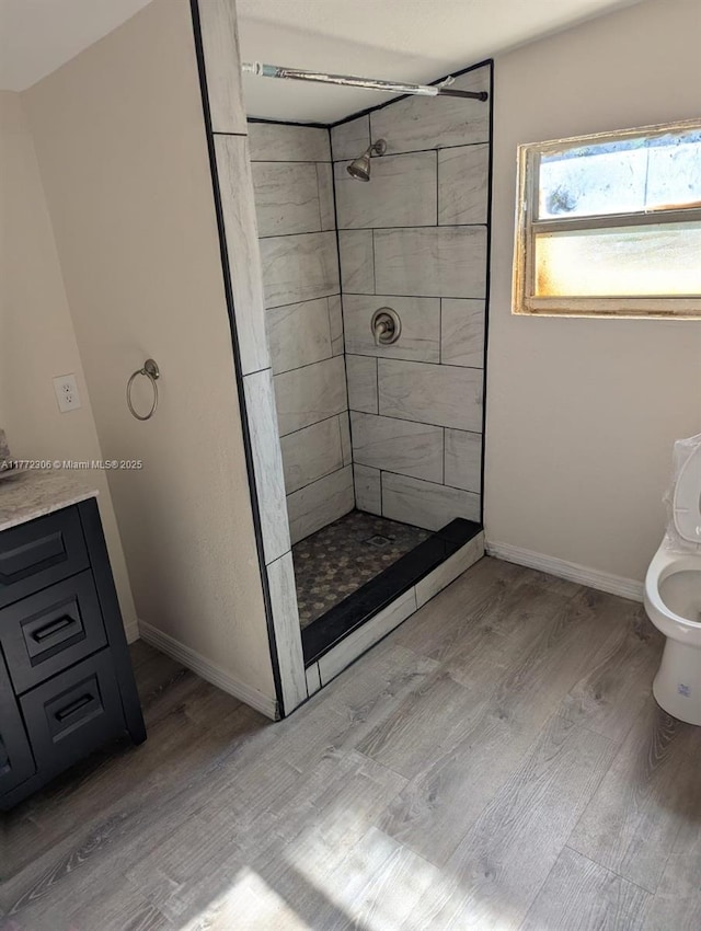 full bathroom with wood finished floors, toilet, a tile shower, and baseboards