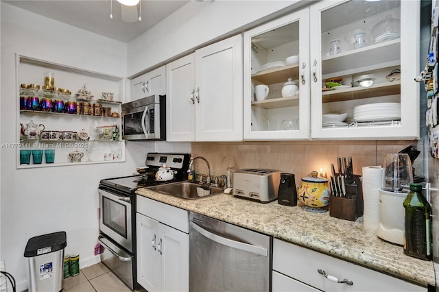 kitchen with appliances with stainless steel finishes, white cabinetry, a sink, glass insert cabinets, and light tile patterned flooring