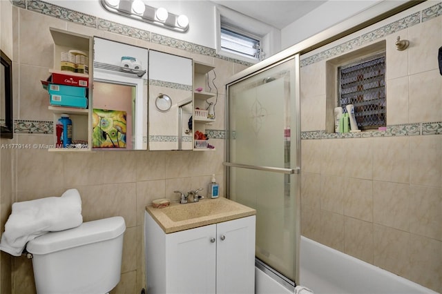 bathroom with toilet, tile walls, combined bath / shower with glass door, and vanity