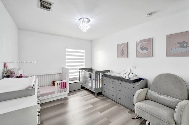 bedroom with visible vents, a nursery area, and light wood-style flooring