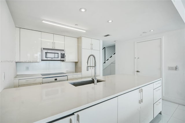 kitchen with stainless steel microwave, light countertops, white cabinetry, cooktop, and a sink