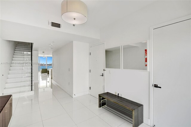 corridor with visible vents, baseboards, stairway, and light tile patterned floors